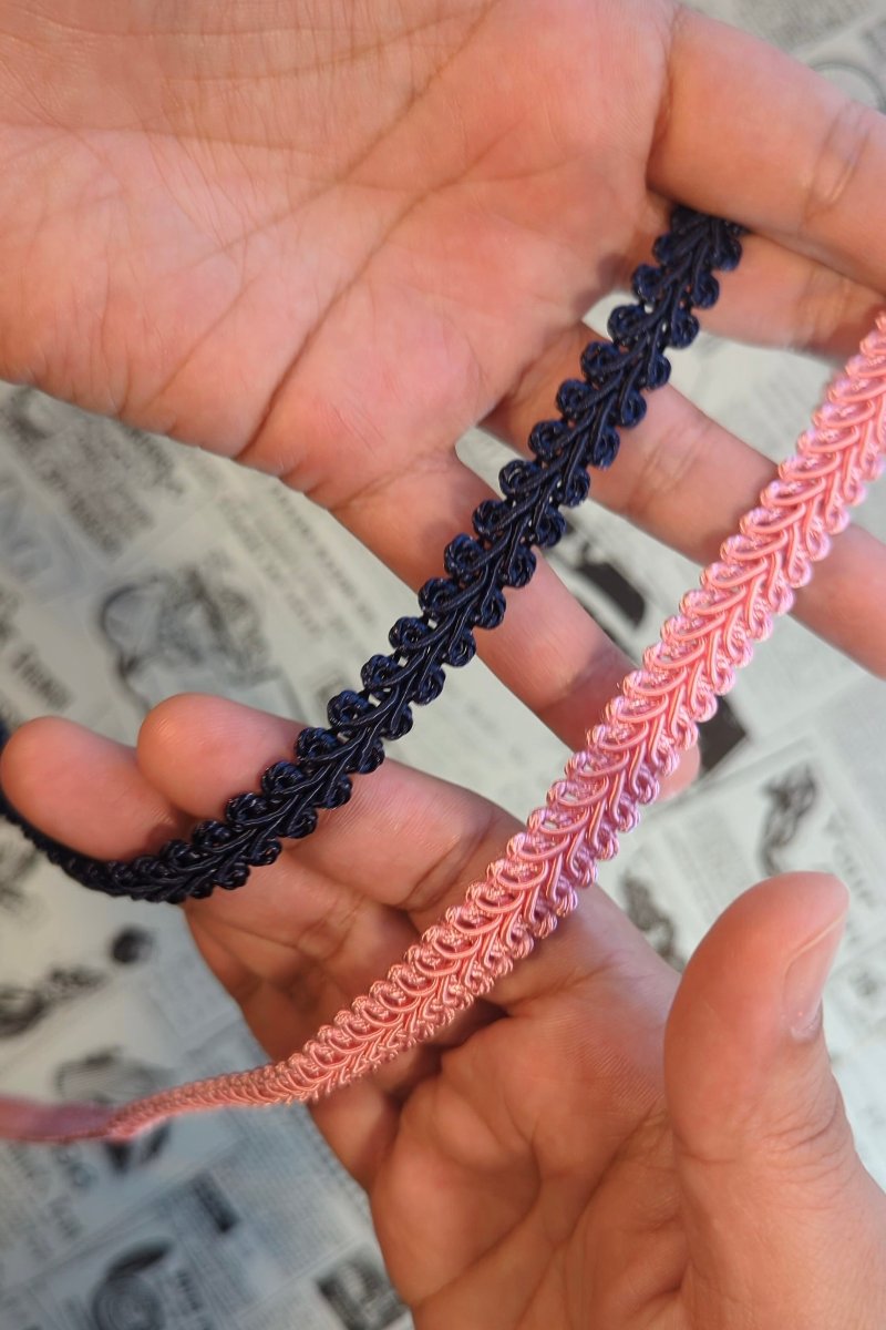 A close-up of the artists' hands handling a navy and a pink braid trim. 