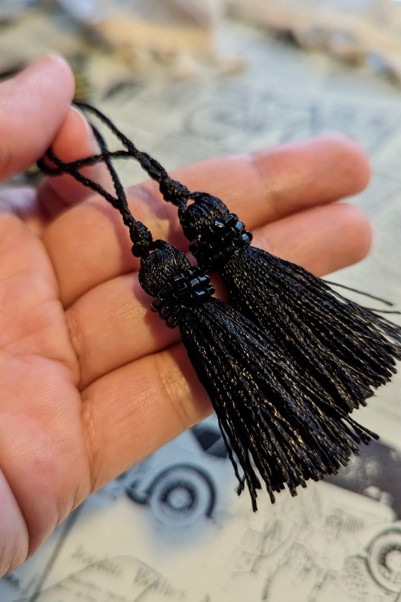 A closeup of the artists' hand holding two black beaded tassels.